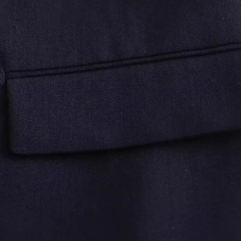 Close-up do bolso frontal com lapela do blazer feminino azul-marinho, destacando a costura e a textura do tecido.
