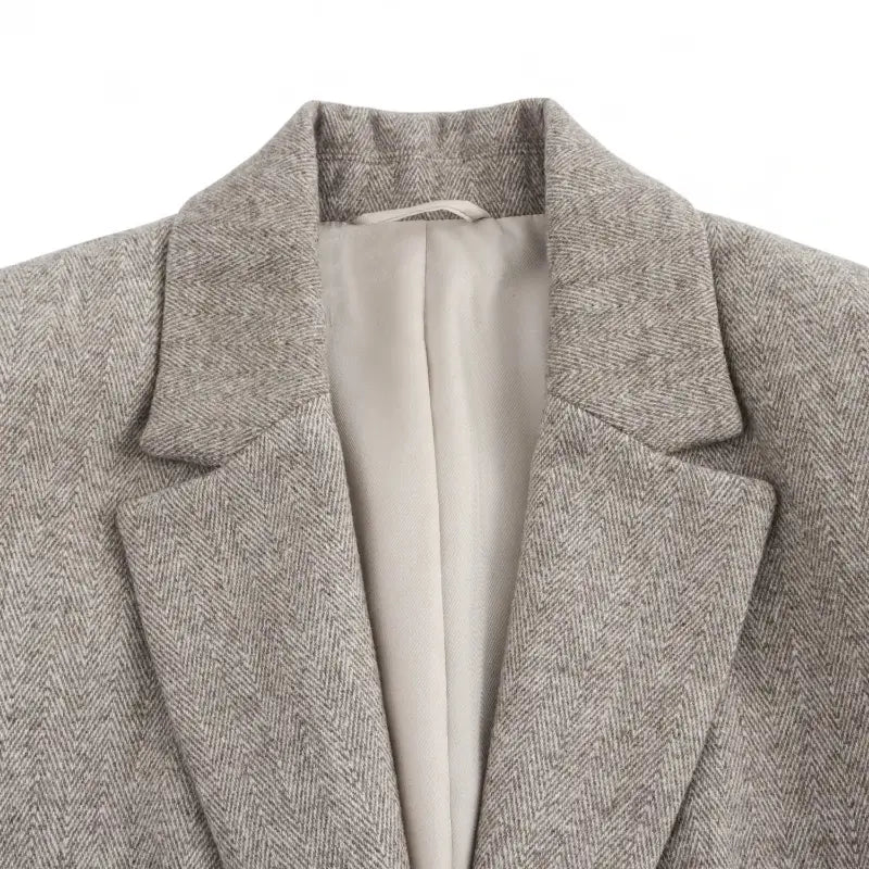 Close-up da gola e lapelas entalhadas do blazer feminino bege, destacando a textura da peça e o forro interno.