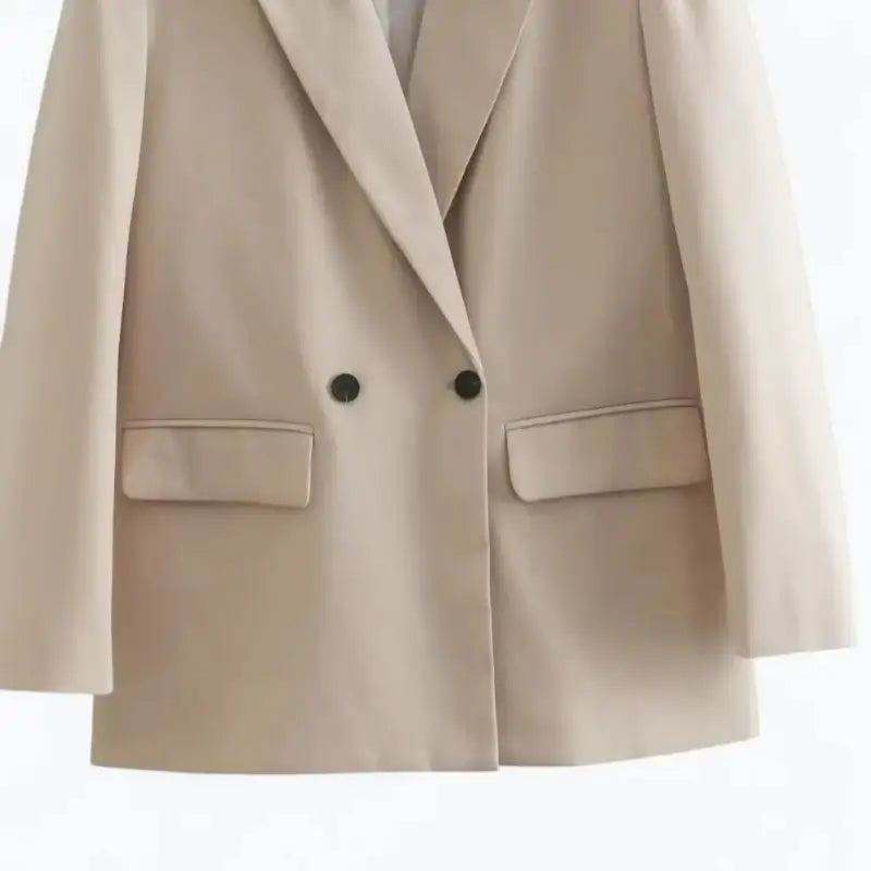 Close-up da parte inferior do blazer feminino bege, com botões e bolsos frontais com lapela.