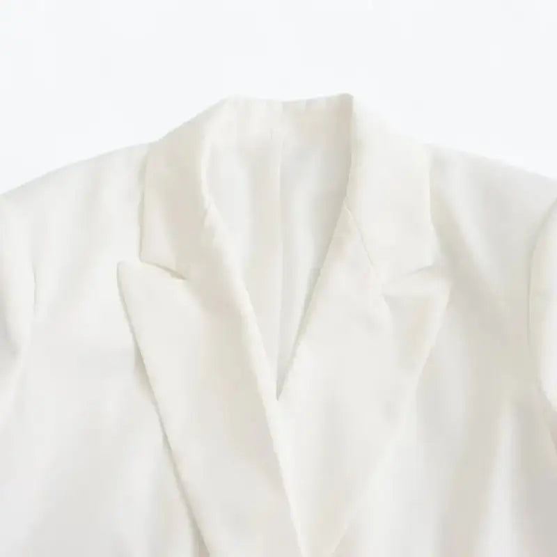 Close-up da gola e lapelas entalhadas do blazer feminino branco, destacando a textura do tecido e o forro interno.