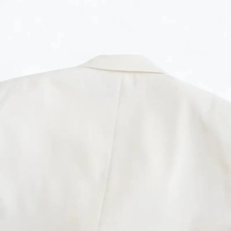 Close-up da gola e parte superior das costas do blazer feminino branco, destacando a costura vertical central.