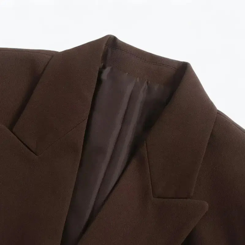 Close-up da gola e lapelas entalhadas do blazer feminino marrom, destacando a textura do tecido e o forro interno.