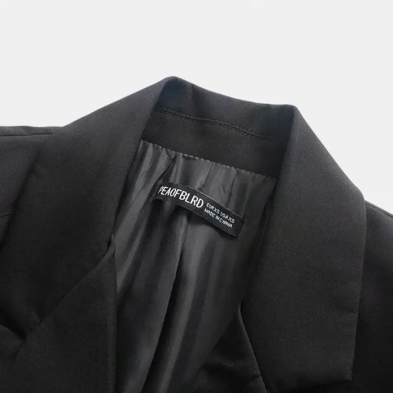 Close-up da gola e lapelas entalhadas do blazer feminino preto, destacando a textura do tecido e o forro interno.