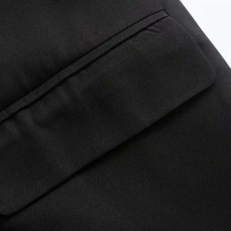 Close-up do bolso frontal com lapela do blazer feminino preto, destacando a costura e a textura do tecido.