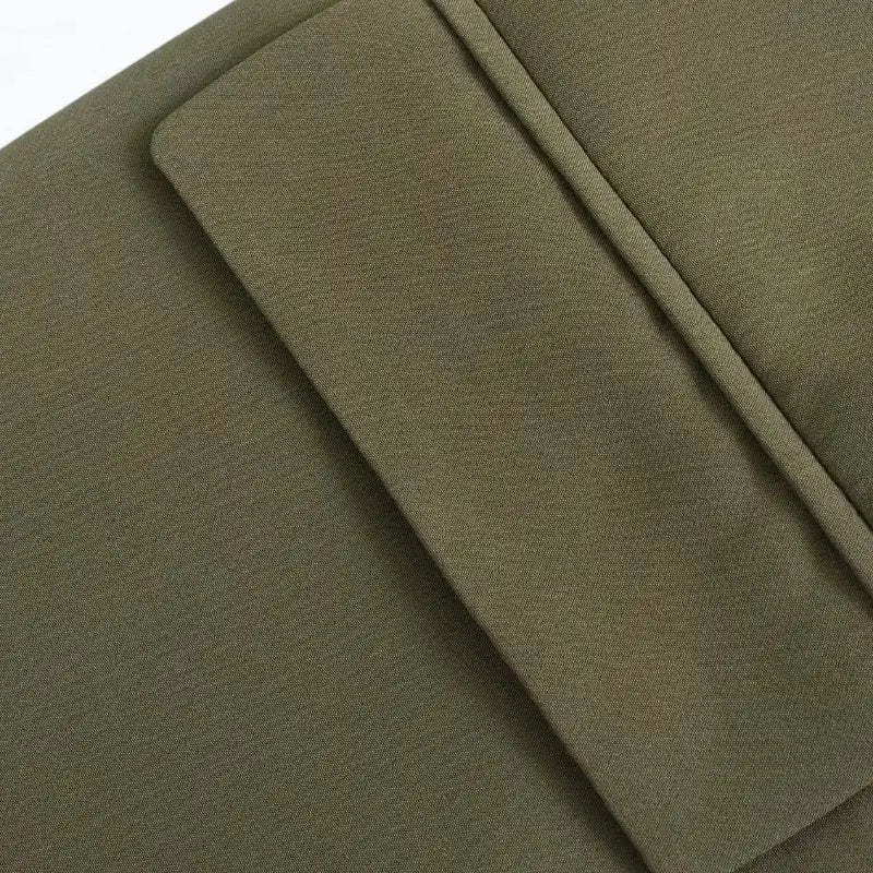 Close-up do bolso frontal com lapela do blazer feminino verde, destacando a costura e a textura do tecido.