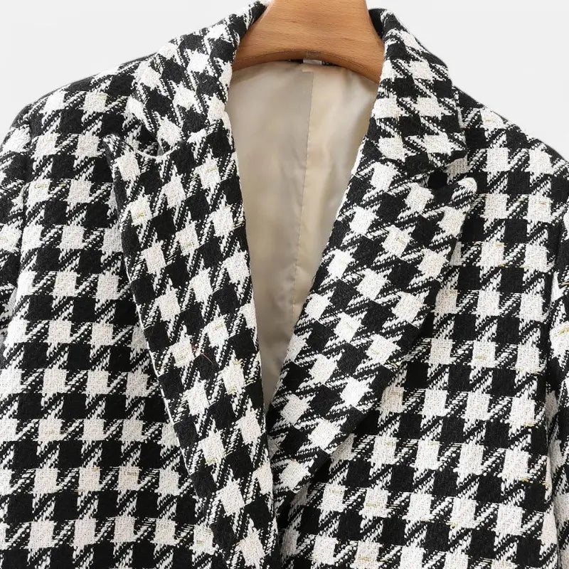Close-up da gola e lapelas entalhadas do blazer feminino alongado com estampa xadrez preto e branco, destacando o padrão miúdo e o forro creme.