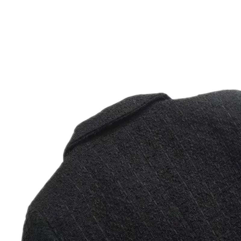 Close-up da parte superior traseira da gola e ombro do blazer feminino de tweed preto, destacando a textura característica do tecido.