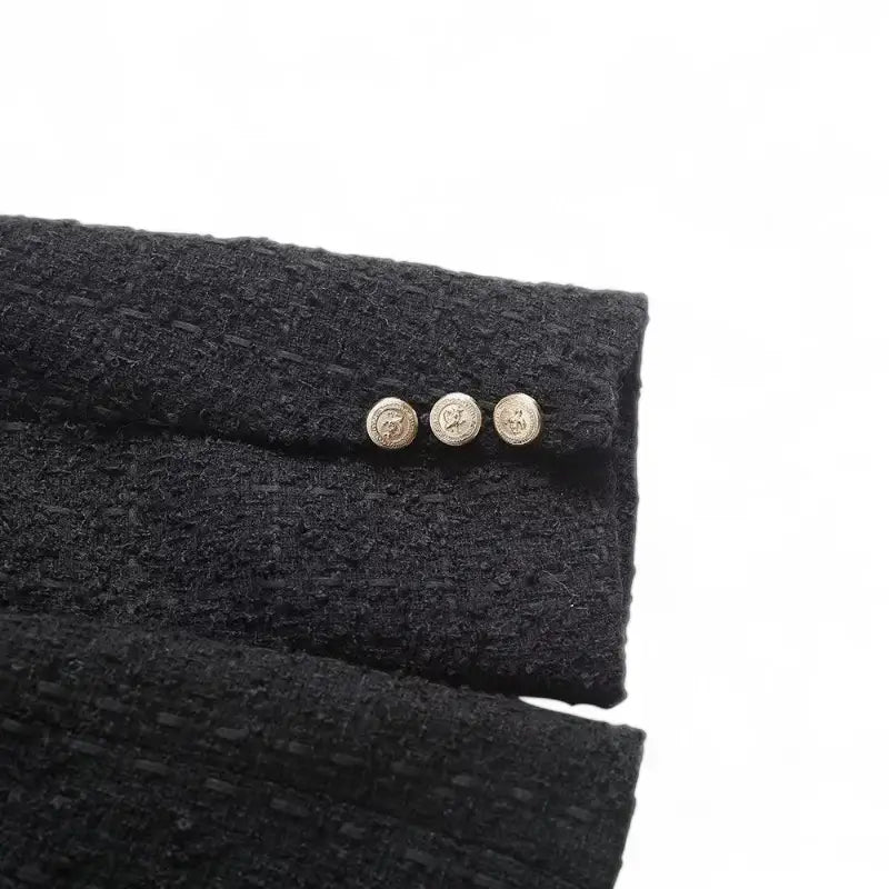 Close-up da parte traseira do punho da manga do blazer feminino de tweed preto, detalhando os três botões dourados decorativos.