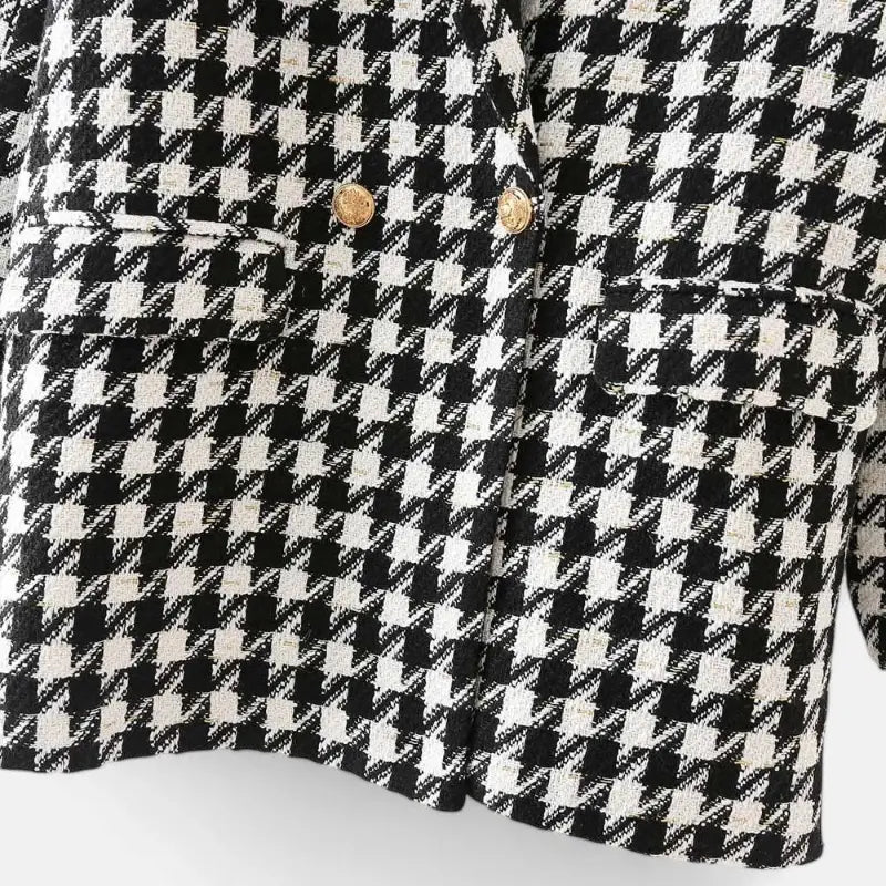 Close-up da parte inferior do blazer feminino alongado com estampa xadrez preto e branco, com botões dourados e bolsos chapados com lapela.
