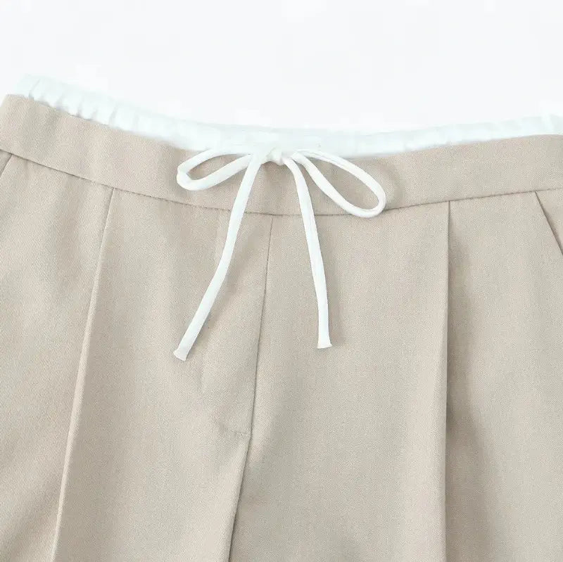 Close-up da cintura alta da calça alfaiataria feminina bege, destacando o cordão de amarração branco.