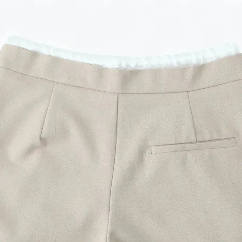 Close-up da cintura traseira da calça alfaiataria feminina bege, com bolso falso embutido traseiro.