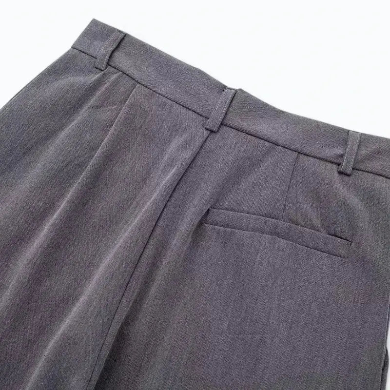 Close-up da cintura traseira da calça feminina cinza, com presilhas de cinto e um bolso falso embutido.