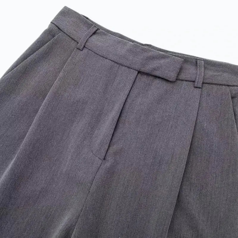 Close-up da cintura alta e pregas frontais da calça feminina cinza, destacando as presilhas de cinto.