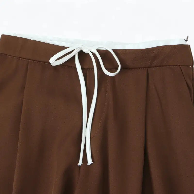 Close-up da cintura alta da calça alfaiataria feminina marrom, destacando o cordão de amarração branco.