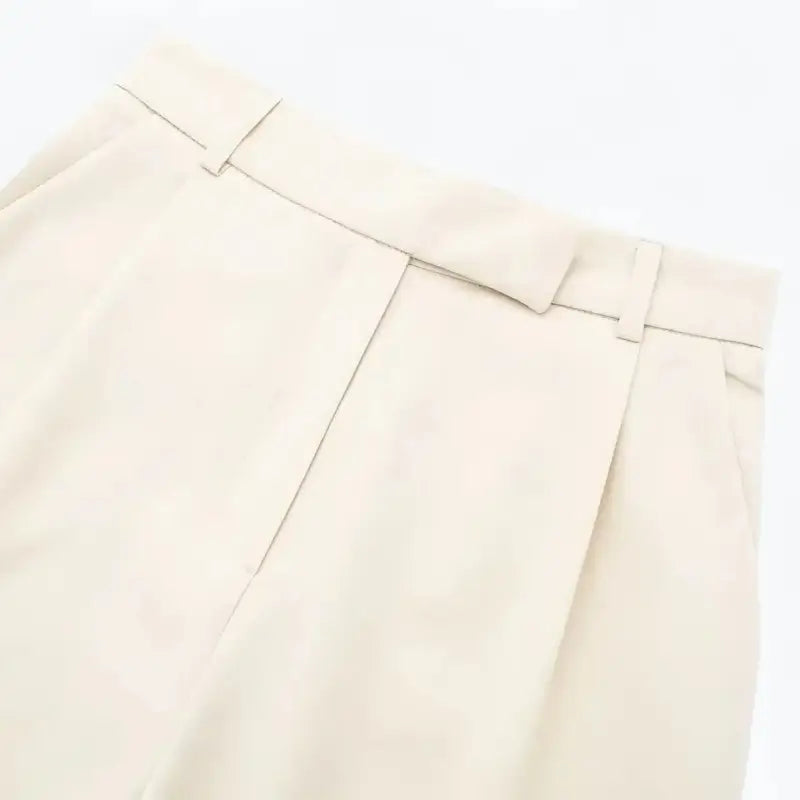 Close-up da cintura alta e pregas frontais da calça feminina off-white, destacando as presilhas de cinto.