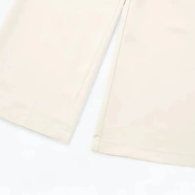 Close-up das pernas largas e da barra da calça alfaiataria feminina off-white, mostrando o caimento fluido.