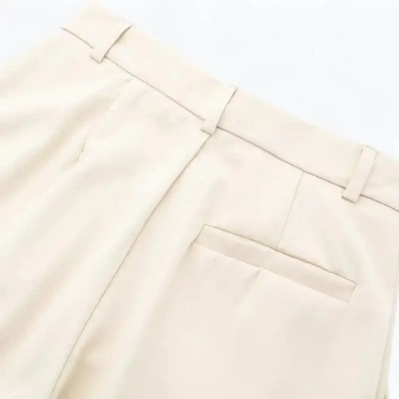 Close-up da cintura traseira da calça feminina off-white, com presilhas de cinto e um bolso falso embutido.
