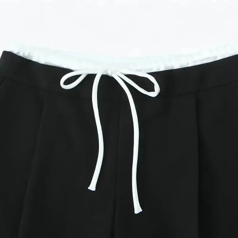 Close-up da cintura alta da calça alfaiataria feminina preta, destacando o cordão de amarração branco.
