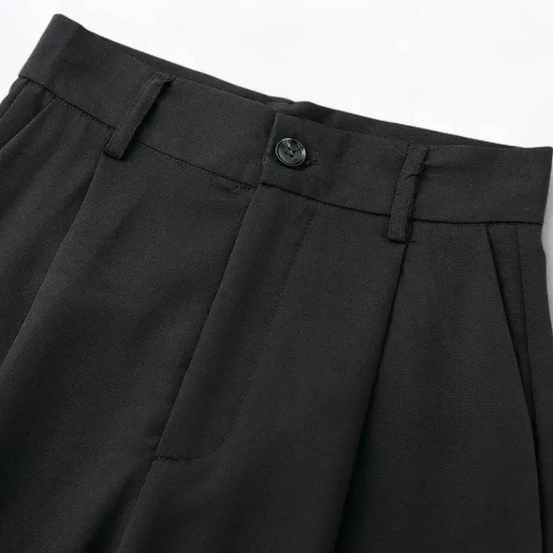 Close-up da cintura alta da calça feminina preta, destacando o botão preto frontal, presilhas de cinto e pregas.