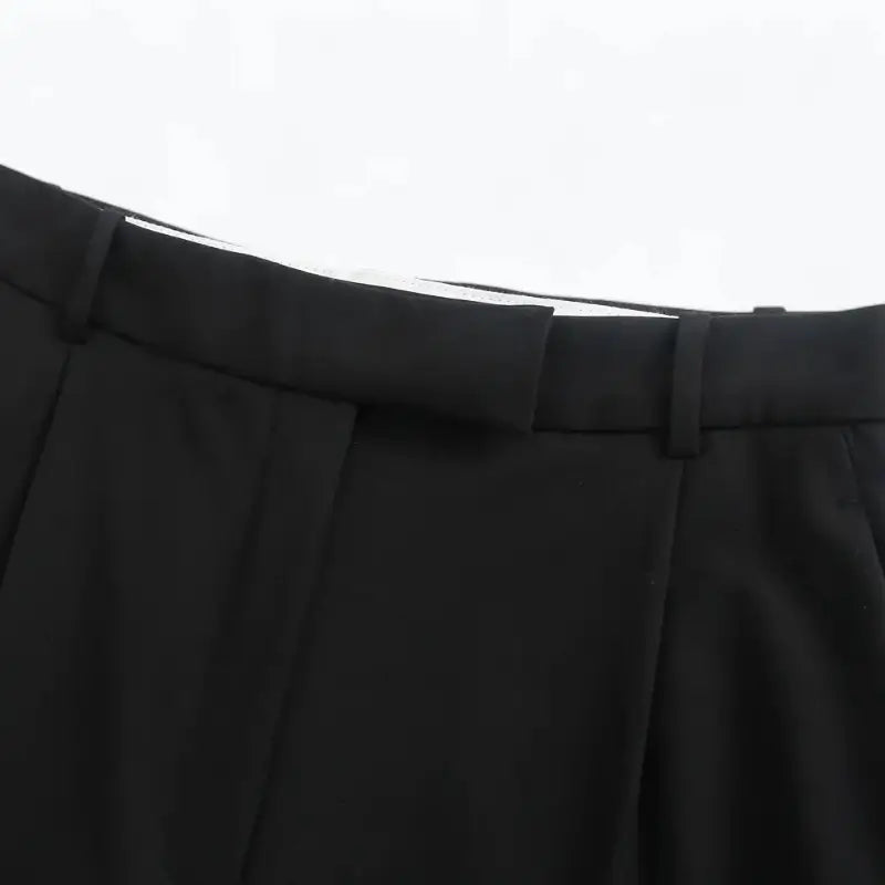 Close-up da cintura alta da calça feminina preta, detalhando as presilhas de cinto e o acabamento do cós.