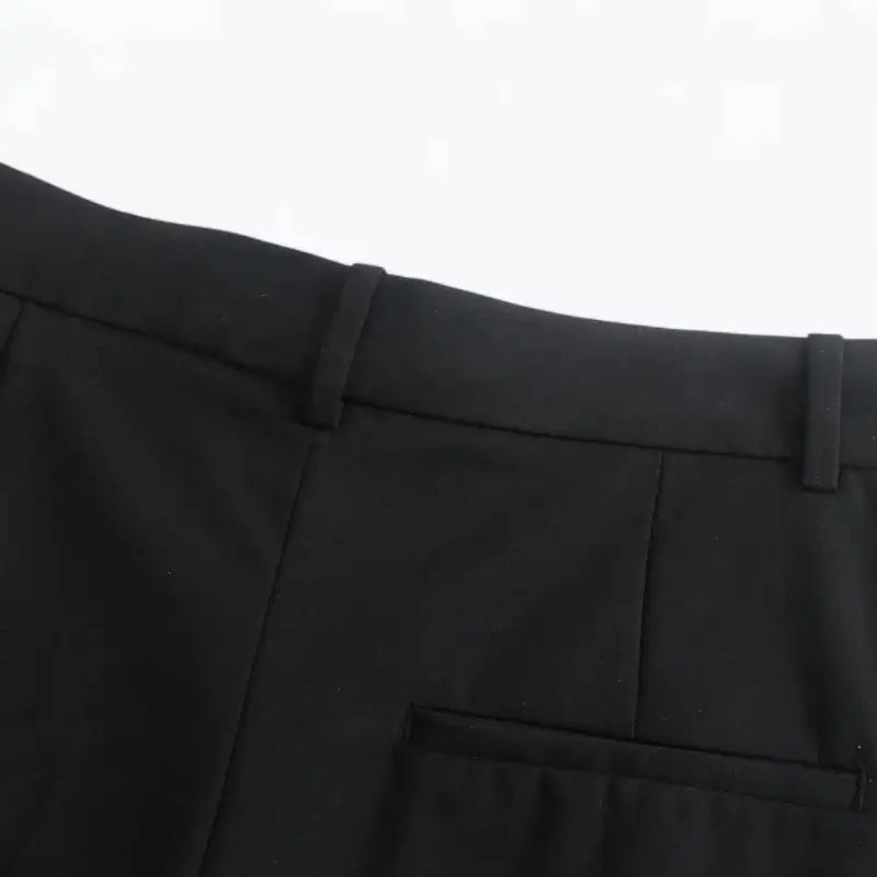 Close-up da cintura traseira da calça feminina preta, com presilhas de cinto e um bolso falso embutido.
