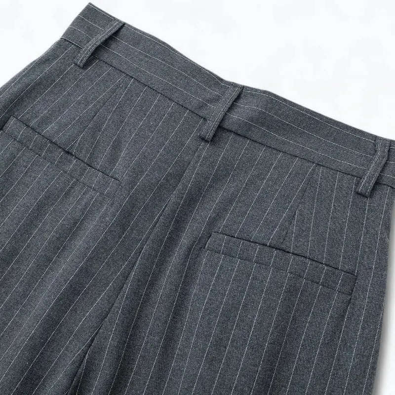 Close-up da cintura traseira da calça feminina de alfaiataria cinza com risca de giz, com presilhas de cinto e bolsos falsos embutidos.