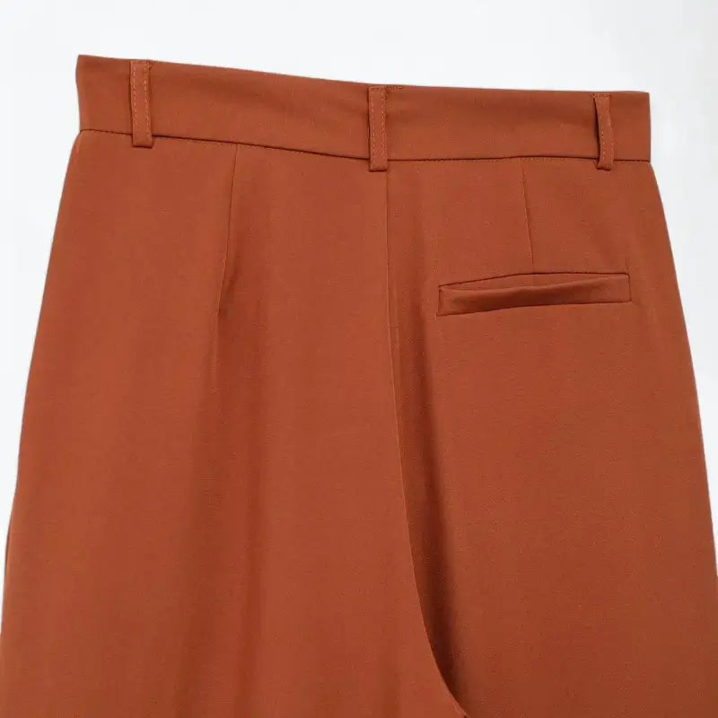 Close-up da cintura traseira da calça feminina terracota, com presilhas de cinto e um bolso falso embutido.