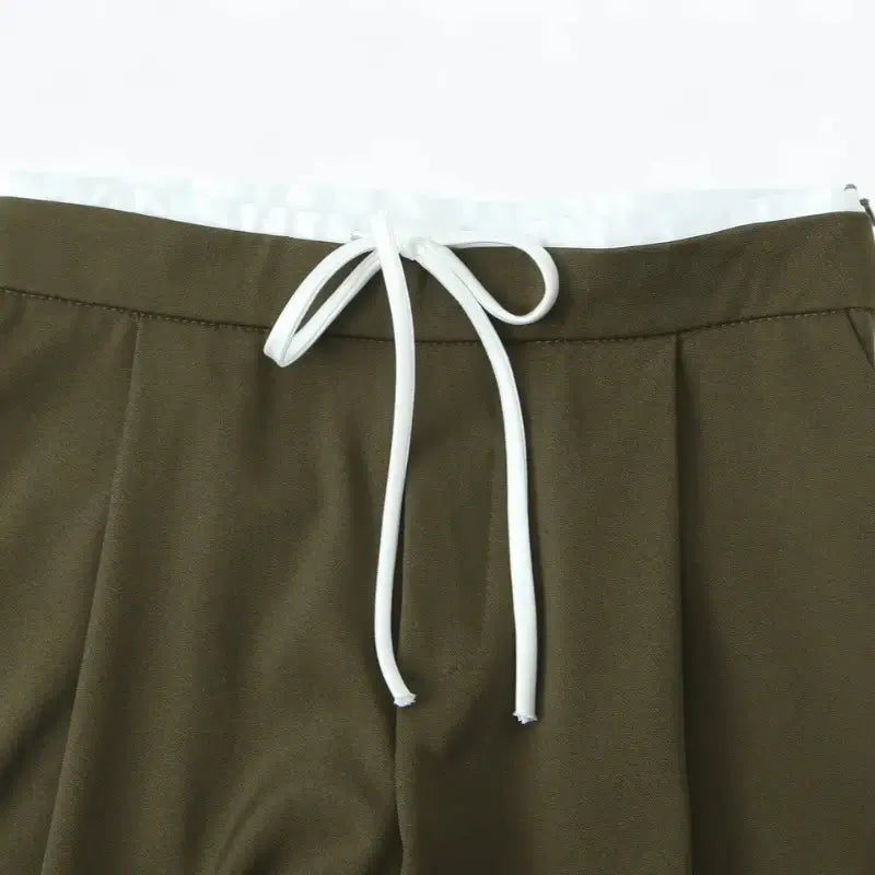 Close-up da cintura alta da calça alfaiataria feminina verde, destacando o cordão de amarração branco.