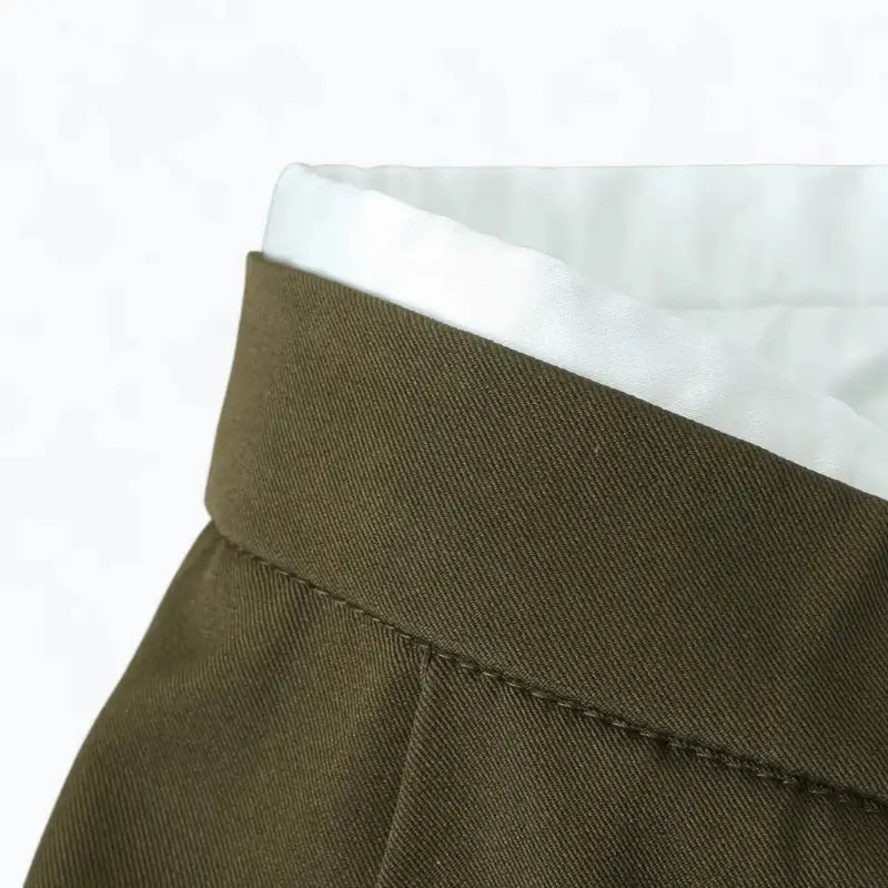 Close-up da cintura da calça feminina de alfaiataria verde, destacando a costura do cós e o detalhe do forro branco.