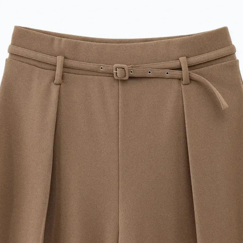 Close-up da cintura alta da calça feminina marrom, destacando o cinto fino com fivelas metálicas e as pregas frontais.