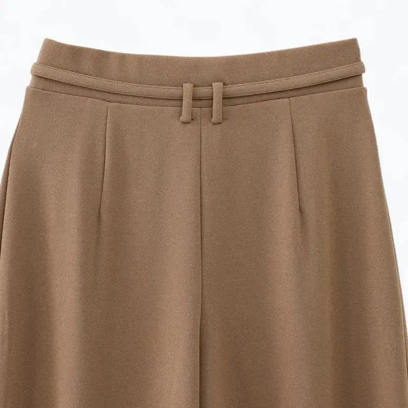 Close-up das pernas largas e da barra da calça pantalona feminina marrom, mostrando o caimento fluido.
