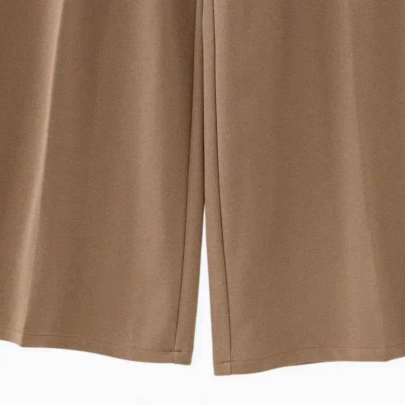 Close-up da parte traseira das pernas largas e da barra da calça pantalona feminina marrom, mostrando o caimento fluido.