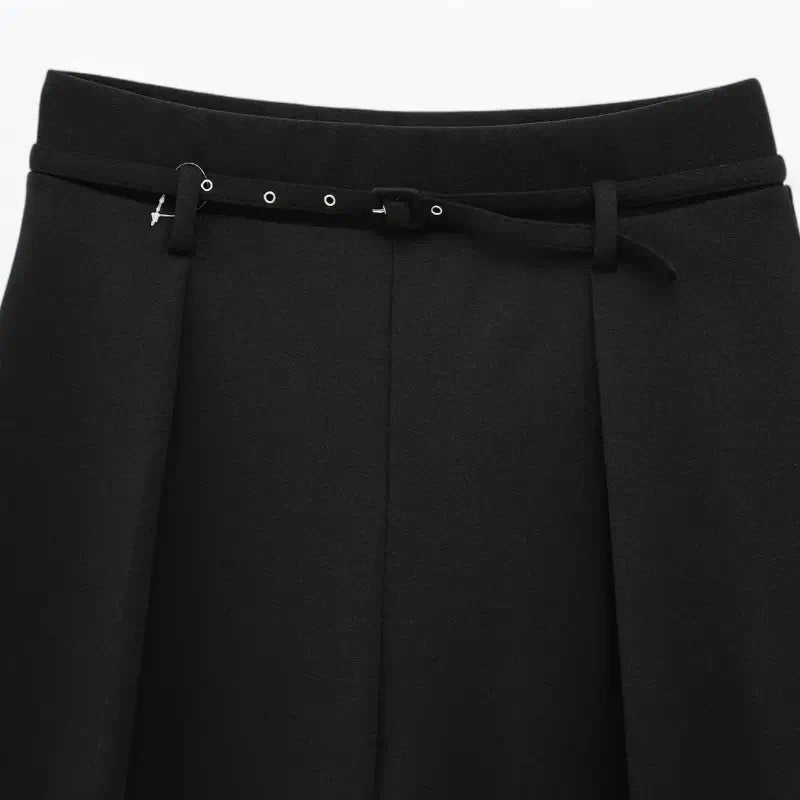 Close-up da cintura alta da calça feminina preta, destacando o cinto fino com fivelas metálicas e as pregas frontais.
