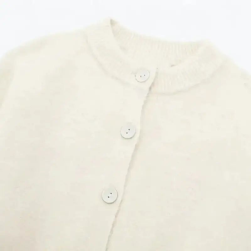 Close-up da gola redonda canelada e botões frontais do cardigan feminino off white, destacando a textura felpuda.