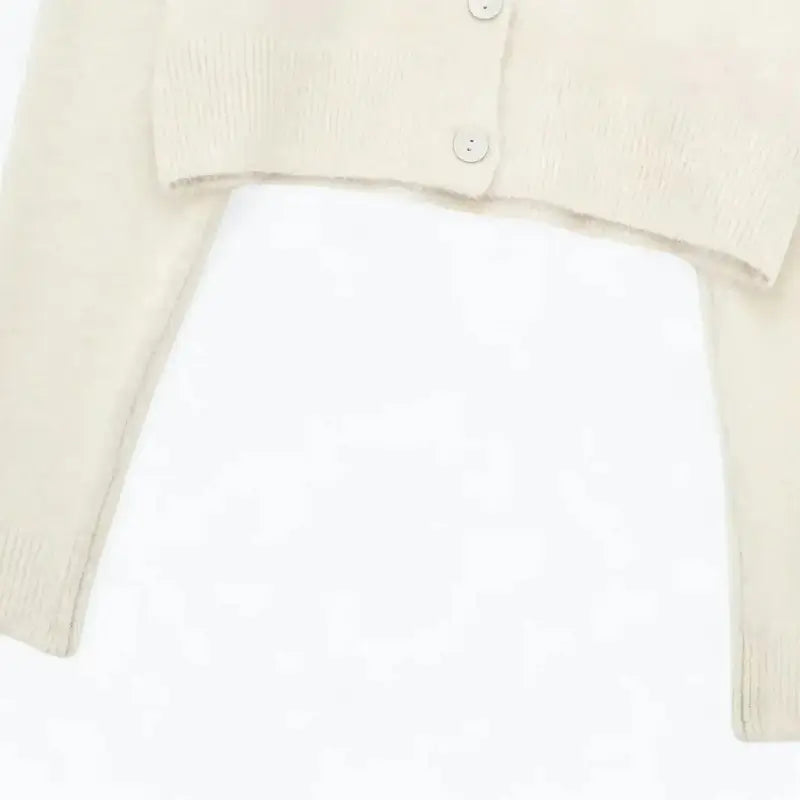 Close-up da barra inferior e botões do cardigan feminino off white, evidenciando a textura felpuda e a barra canelada.