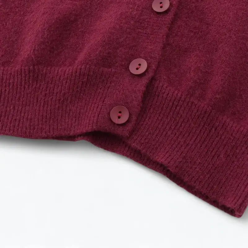 Close-up da barra inferior e botões do cardigan feminino vermelho, evidenciando a textura felpuda e a barra canelada.