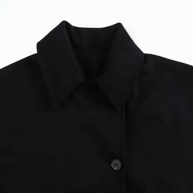 Close-up da gola de camisa e do botão frontal do casaco feminino oversized preto, destacando o design.