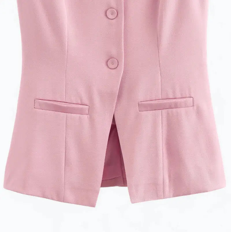 Close-up da parte inferior do colete feminino alongado rosa, com botões, fenda central e bolsos falsos.