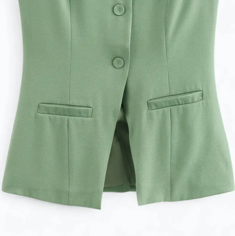 Close-up da parte inferior do colete feminino alongado verde menta, com botões, fenda central e bolsos falsos.