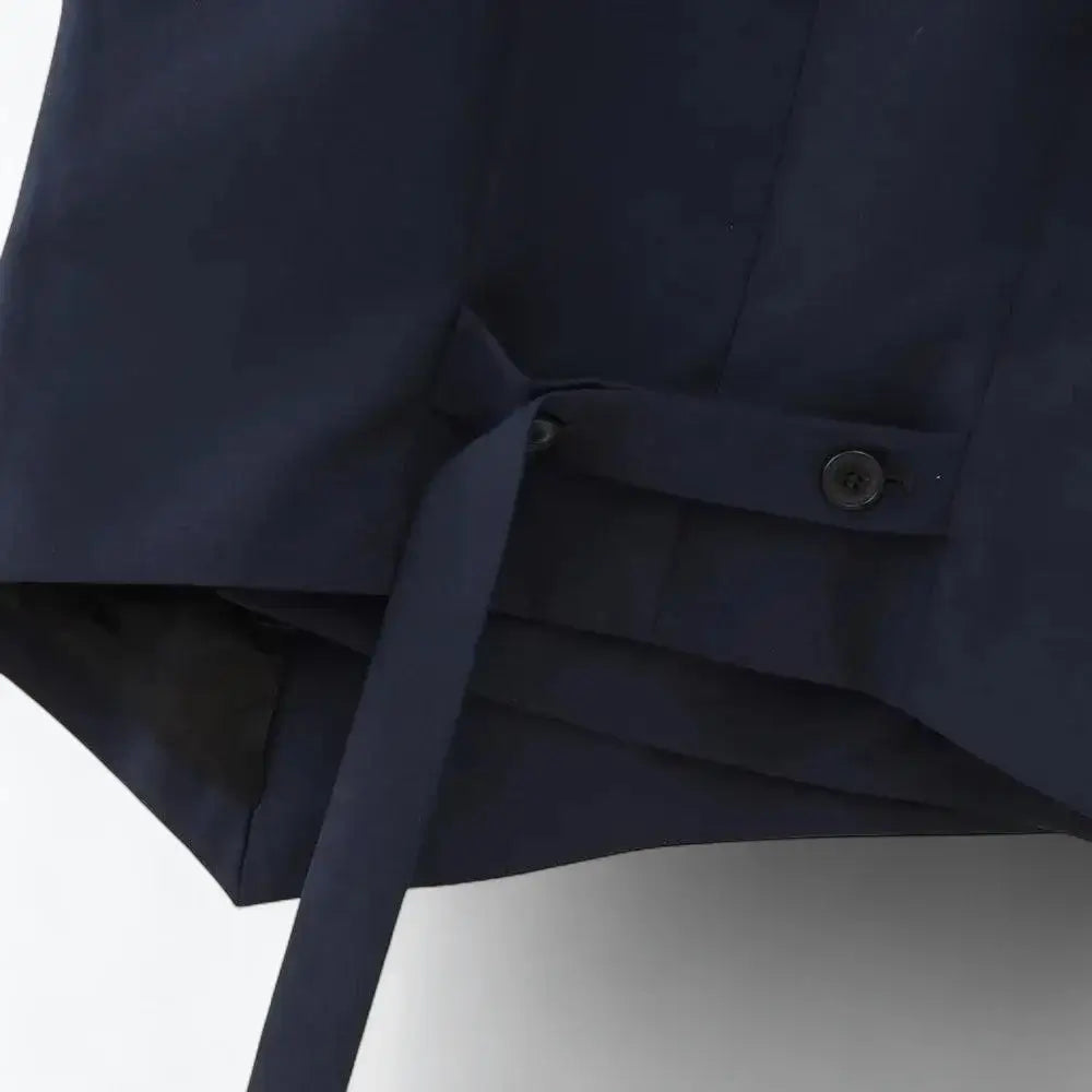 Close-up da alça ajustável com botões pretos na cintura traseira do colete feminino azul marinho.