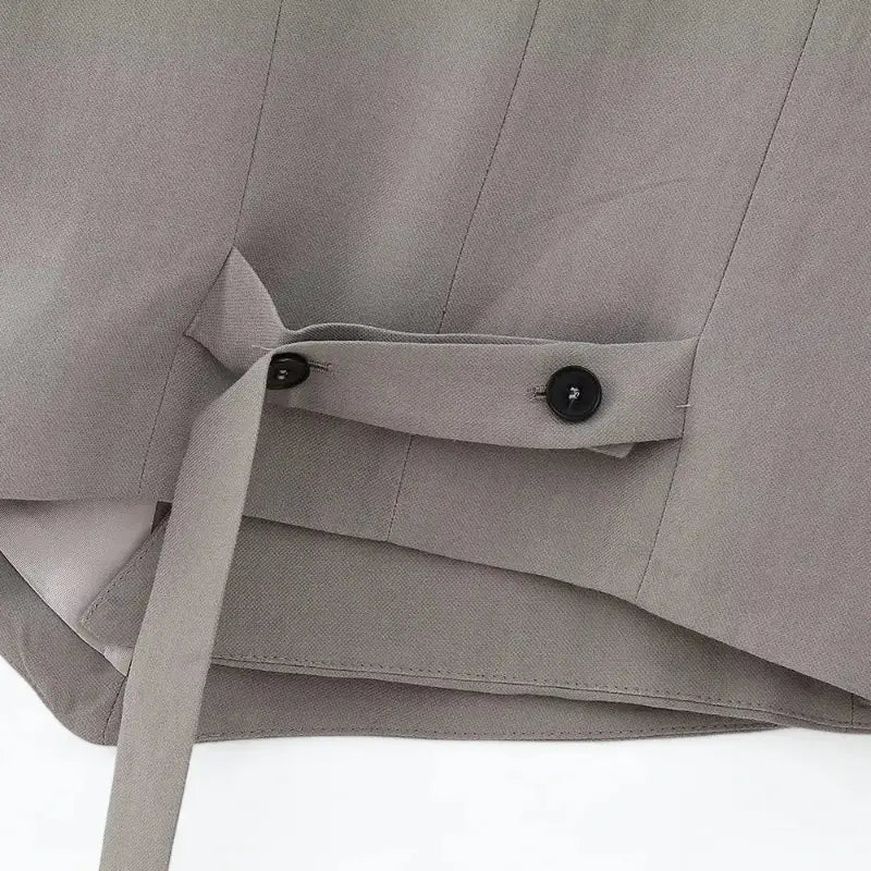 Close-up da alça ajustável com botões pretos na cintura traseira do colete feminino cinza.