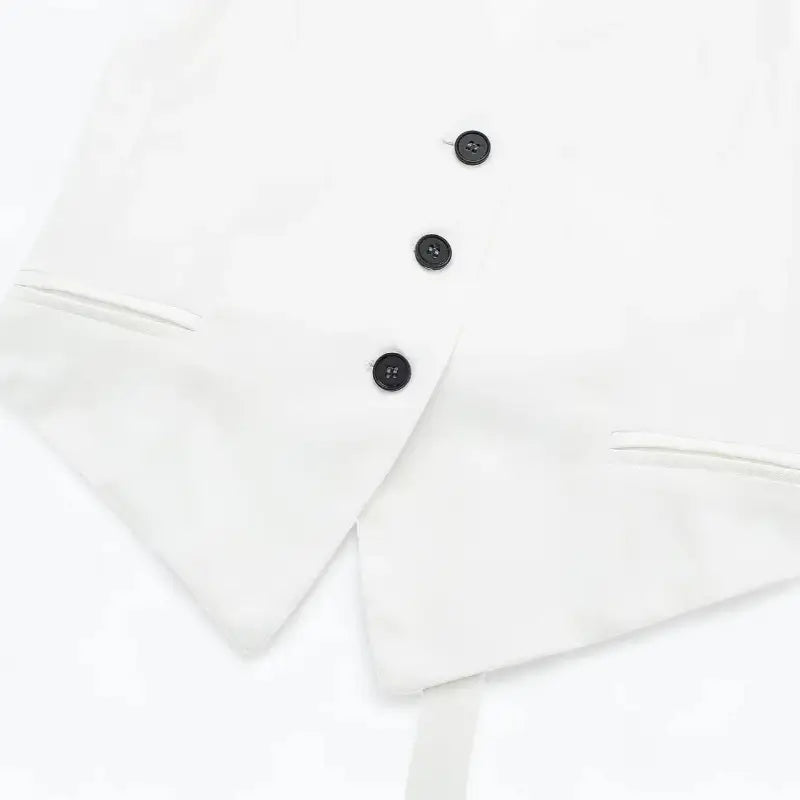 Close-up da parte inferior do colete feminino branco, com botões frontais e bolsos falsos, exibindo a barra pontuda.