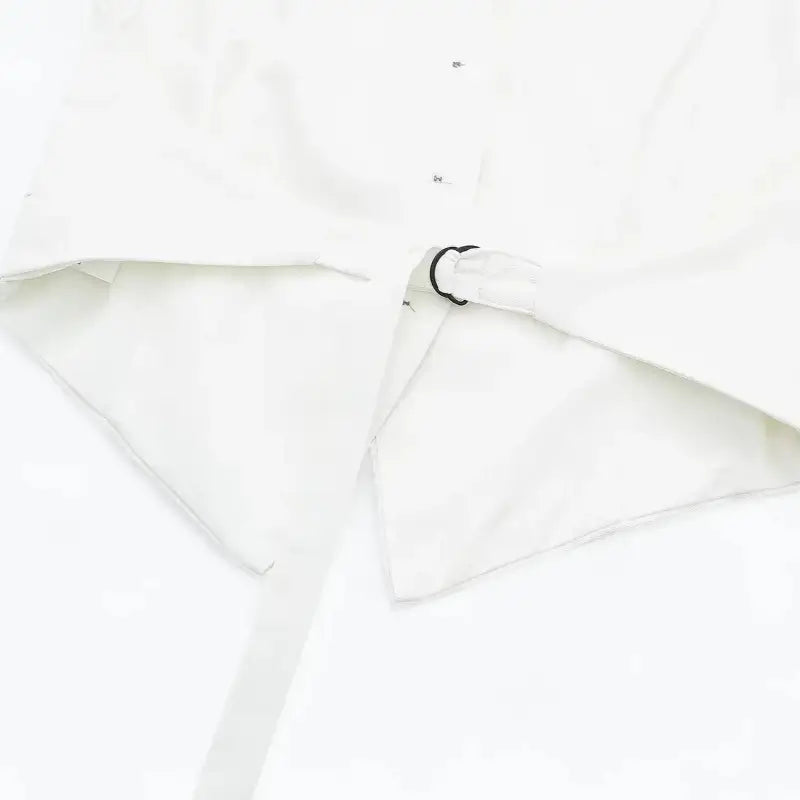Close-up da tira ajustável com fivela anelar preta na cintura do colete feminino branco, com barra pontuda.