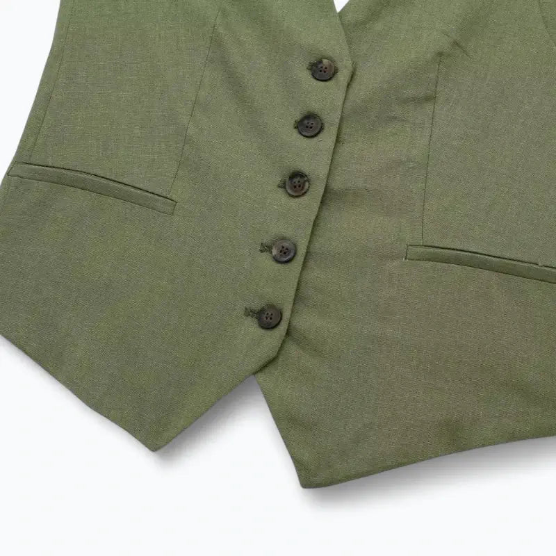 Close-up da parte inferior do colete feminino verde, com cinco botões verdes e bolsos falsos, exibindo a barra pontuda.