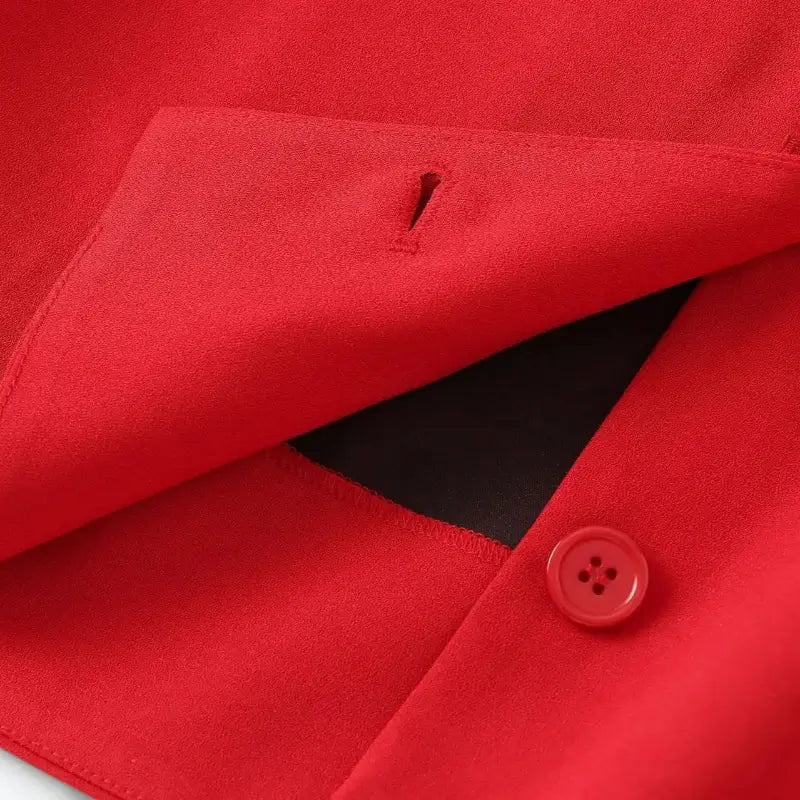 Close-up de uma casa de botão vertical e um botão redondo vermelho em colete feminino de alfaiataria vermelho, mostrando o tecido liso.