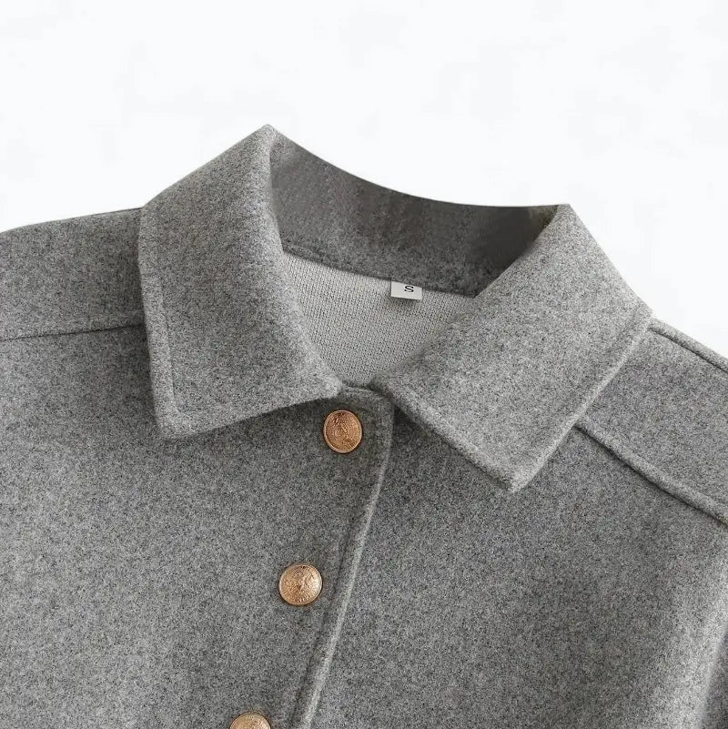 Close-up da gola estilo camisa da jaqueta feminina cinza, destacando três botões dourados e a textura do tecido.