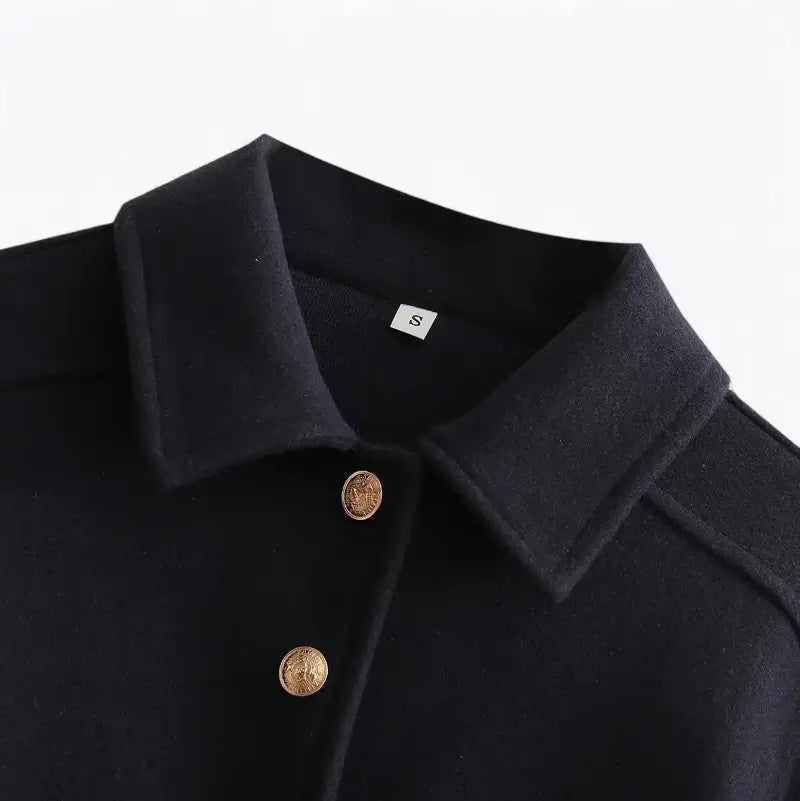 Close-up da gola estilo camisa da jaqueta feminina preta, destacando dois botões dourados e a textura do tecido.