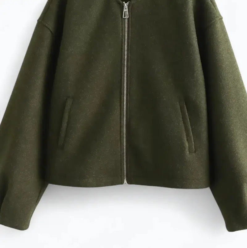 Close-up da parte frontal da jaqueta bomber feminina verde, mostrando o zíper prateado e o os bolsos laterais.