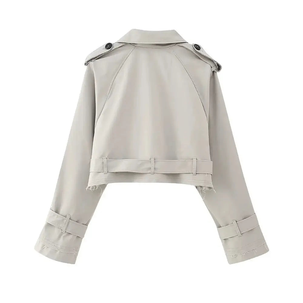 Vista traseira da jaqueta feminina cropped cinza estilo trench coat, com cinto na barra, alças nos ombros e fivelas nos punhos, em fundo branco.