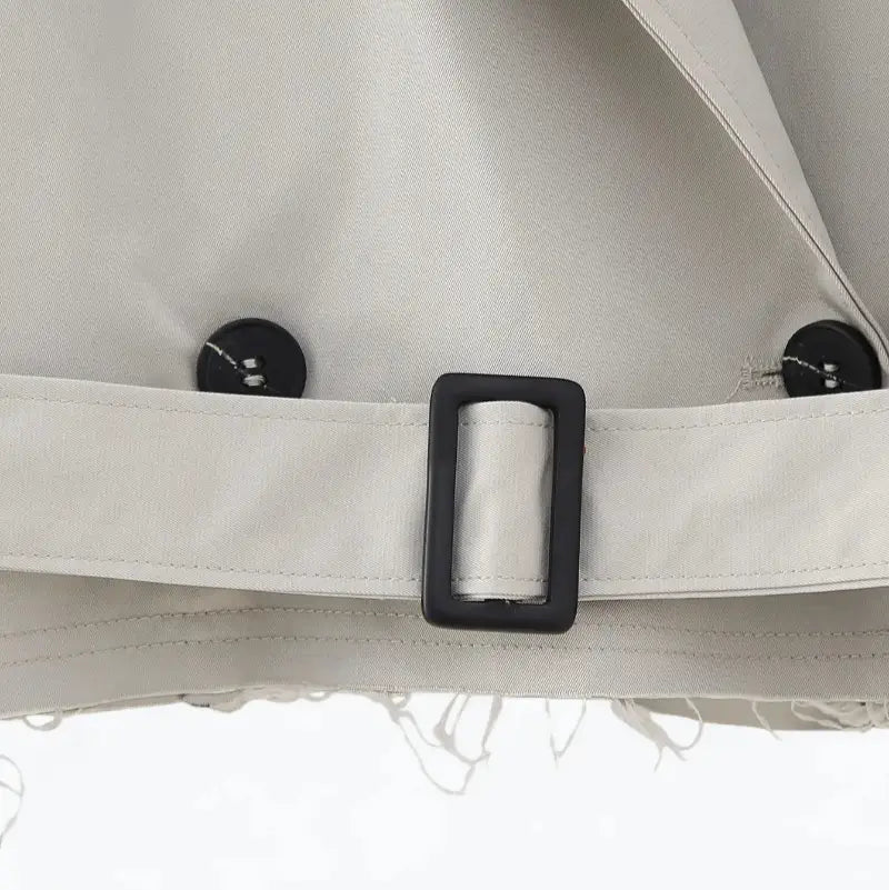 Close-up da barra e do cinto da jaqueta feminina cropped cinza estilo trench coat, mostrando o abotoamento duplo e a fivela preta.